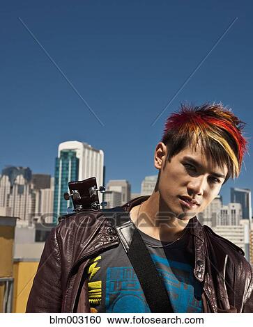 Stock Image - Asian man with guitar on urban rooftop. Fotosearch