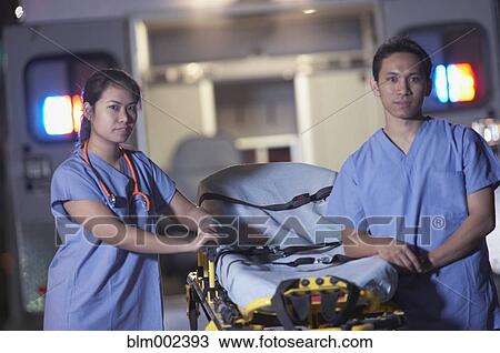 Stock Image - Asian medical professionals standing next to gurney. Fotosearch