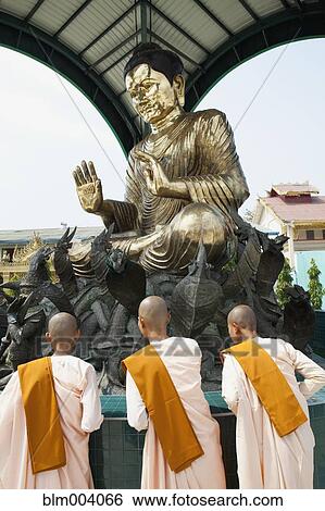 Stock Photograph - Asian monks standing below statue. Fotosearch