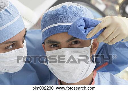 Stock Image - Asian nurse wiping doctor's brow. Fotosearch