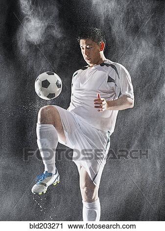 Stock Image - Asian soccer player kicking ball in rain. Fotosearch