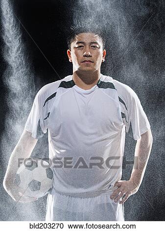 Stock Image - Asian soccer player standing in rain. Fotosearch