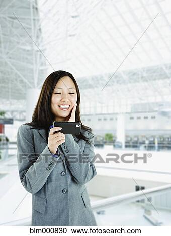 Stock Image - Asian woman checking cell phone in airport. Fotosearch