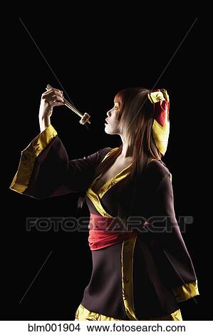 Picture - Asian woman in traditional clothing holding sushi on chopsticks. Fotosearch