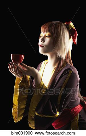 Stock Image - Asian woman in traditional clothing holding tea cup. Fotosearch
