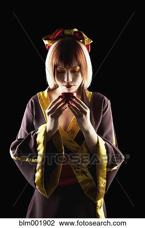 Stock Image - Asian woman in traditional clothing holding tea cup. Fotosearch