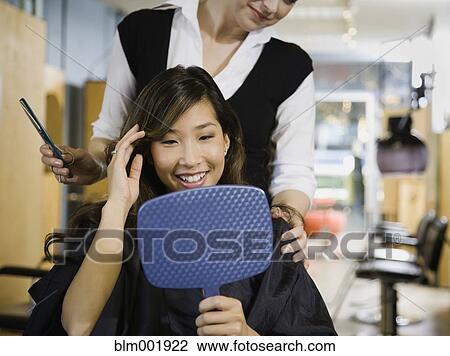 Stock Image - Asian woman looking at hair in salon. Fotosearch