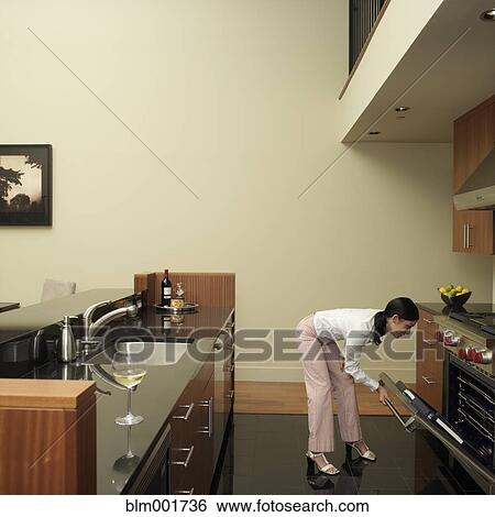 Stock Photograph - Asian woman looking in oven. Fotosearch