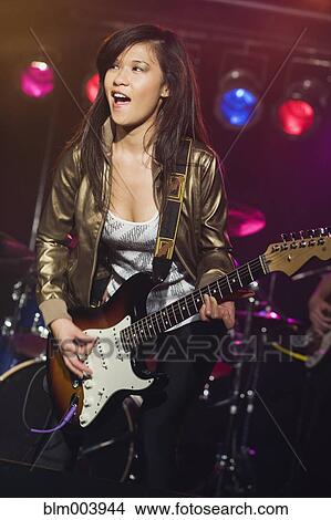 Picture - Asian woman playing electric guitar onstage. Fotosearch