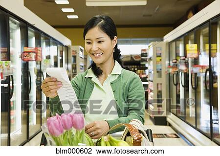Stock Image - Asian woman reading list in grocery store. Fotosearch