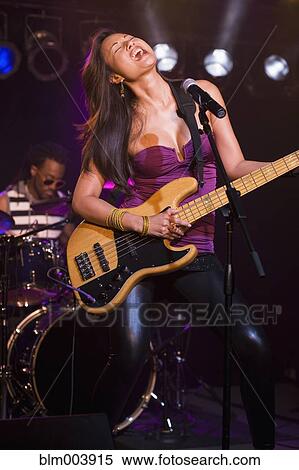 Stock Photography - Asian woman singing and playing electric guitar onstage. Fotosearch