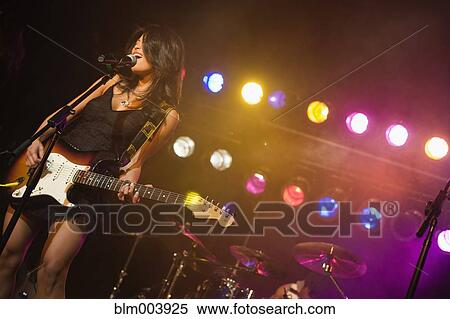 Stock Photography - Asian woman singing and playing electric guitar onstage. Fotosearch