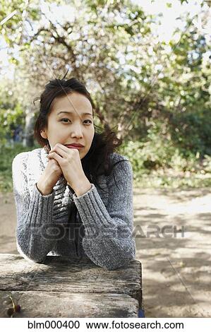 Stock Image - Asian woman sitting at picnic bench. Fotosearch