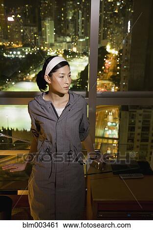 Stock Image - Asian woman standing by window. Fotosearch