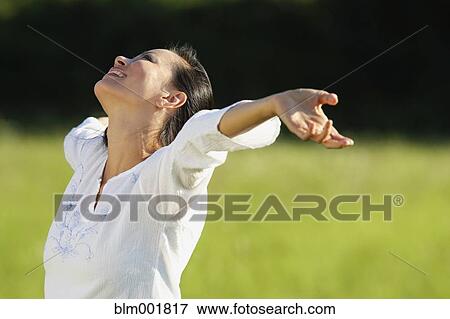 Stock Photo - Asian woman standing in meadow with arms outstretched. Fotosearch