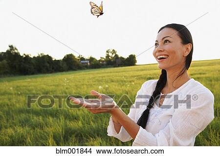 Picture - Asian woman watching butterfly in meadow. Fotosearch