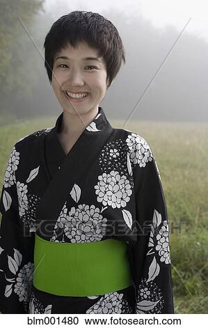 Stock Image - Asian woman wearing traditional robe standing in field. Fotosearch