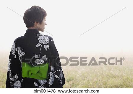 Stock Photo - Asian woman wearing traditional robe standing in field. Fotosearch