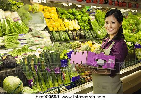 Stock Photo - Asian woman working in produce section of grocery store. Fotosearch