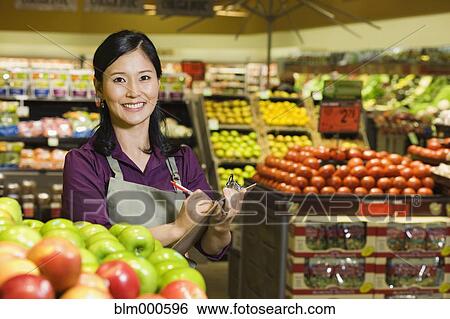 Stock Photograph - Asian woman working in produce section of grocery store. Fotosearch
