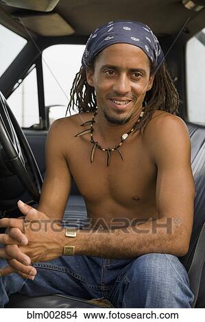 Picture - Bare chested Hispanic man sitting in cab of truck. Fotosearch