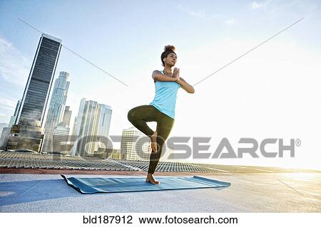 Stock Image - Black woman practicing yoga on urban rooftop. Fotosearch