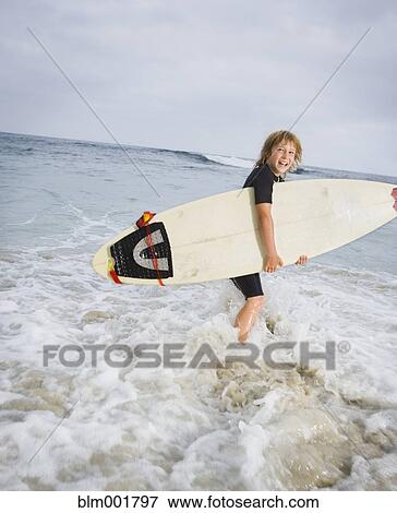 Stock Photo - Boy holding surfboard in surf at beach. Fotosearch