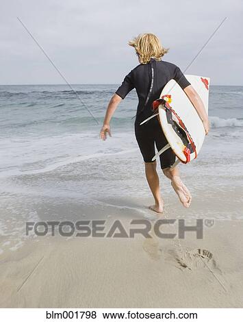 Stock Photo - Boy running with surfboard at beach. Fotosearch