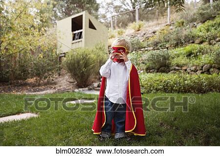 Stock Image - Boy wearing cape and mask in backyard. Fotosearch