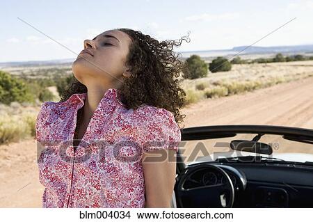 Picture - Breeze blowing on mixed race woman sitting on convertible. Fotosearch