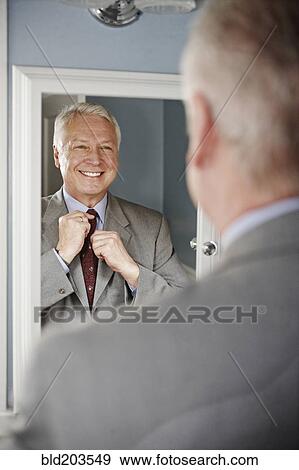 Stock Photo - Businessman adjusting his tie in mirror. Fotosearch