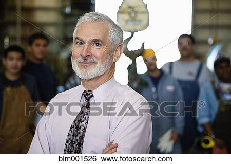 Stock Photograph - Businessman in warehouse with workers in background . Fotosearch