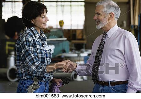 Stock Image - Businessman shaking hands with female warehouse worker. Fotosearch