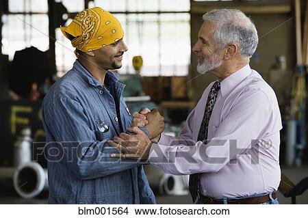 Picture - Businessman shaking hands with male warehouse worker. Fotosearch