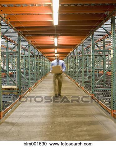 Stock Image - Businessman walking with box in warehouse. Fotosearch