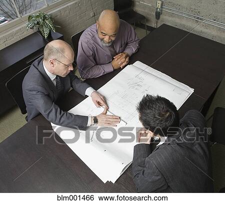 Stock Photograph - Businessmen reviewing blueprints in meeting. Fotosearch