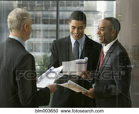 Stock Image - Businessmen reviewing document in office. Fotosearch