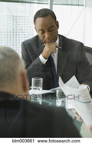 Stock Image - Businessmen reviewing document in meeting. Fotosearch