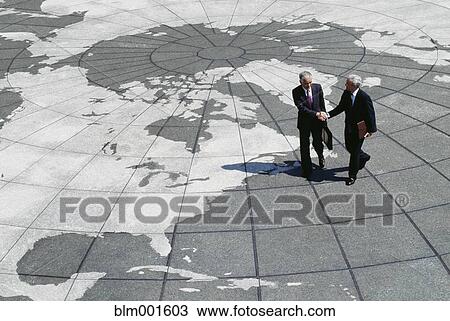 Stock Image - Businessmen shaking hands on map of globe. Fotosearch