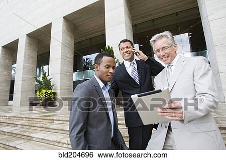 Businessmen using tablet computer on city street View Large Photo Image Stock Photograph - Businessmen using tablet computer on city street. Fotosearch