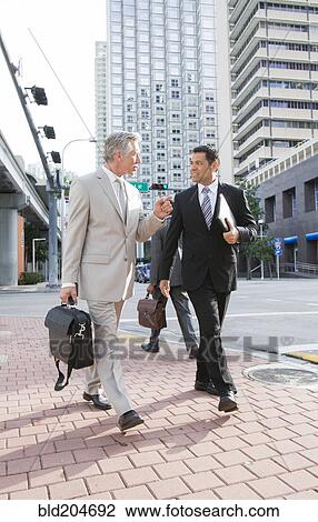 Stock Image - Businessmen walking together on city street. Fotosearch