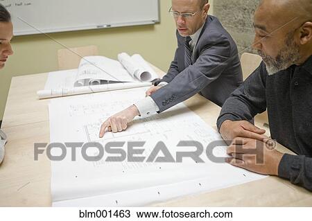 Stock Image - Businesspeople reviewing blueprints in meeting. Fotosearch