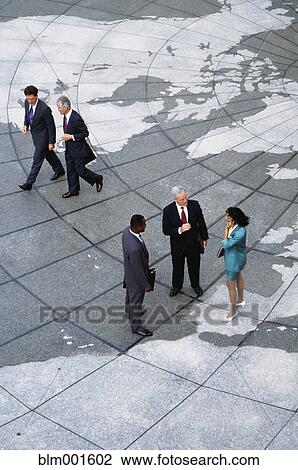 Stock Image - Businesspeople standing on map of globe. Fotosearch