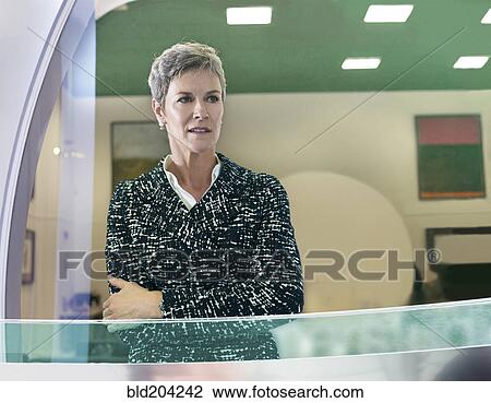 Stock Image - Businesswoman standing at office window. Fotosearch