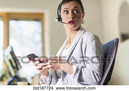 Picture - Businesswoman using cell phone and headset in office. Fotosearch