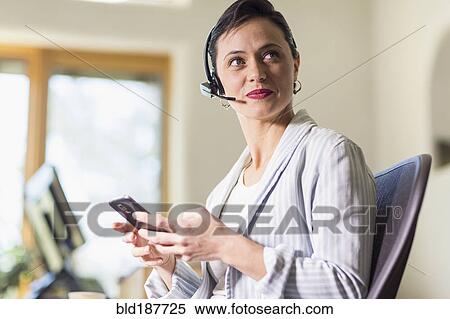 Businesswoman using cell phone and headset in office View Large Photo Image Stock Photography - Businesswoman using cell phone and headset in office. Fotosearch