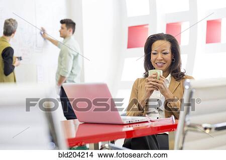 Picture - Businesswoman using laptop in office. Fotosearch