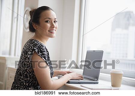 Stock Image - Businesswoman working on laptop in office. Fotosearch