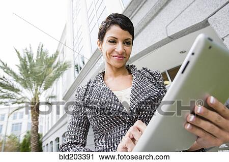 Stock Image - Cape Verdean businesswoman using tablet computer outdoors. Fotosearch