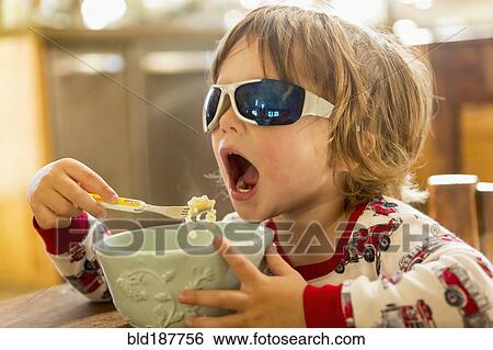 Stock Photograph - Caucasian boy in sunglasses eating in kitchen. Fotosearch